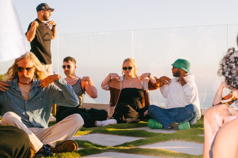 Contact improv circle on the grass at golden hour, hands on shoulders