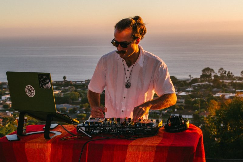 Scott Welch DJing at the decks at sunset, ocean in the background