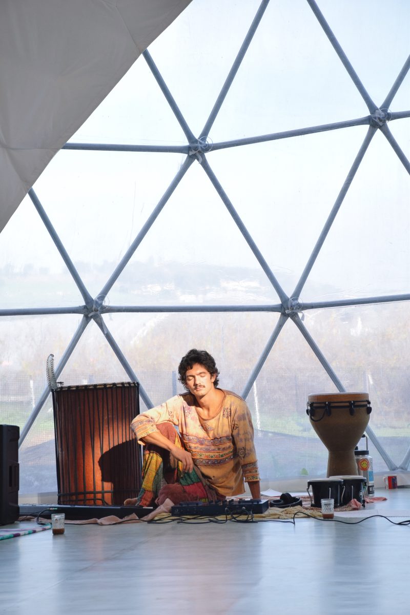 Scott Welch seated with drums and a controller inside the Peace Dome at golden hour